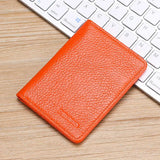 Posé sur un clavier d'ordinateur et sur une table en bois marron clair se trouve le porte carte pour femme en cuir orange.