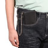 Le modèle en cuir noir est dans une poche de pantalon, attaché avec sa chaîne à un espace du même pantalon.