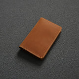 Porte cartes en cuir de vachette pleine fleur marron clair posé sur une surface noire.