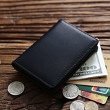 Porte cartes en cuir noir avec des billets, des cartes et pièces de monnaie posés à côté.