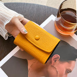 Le porte carte en cuir jaune est tenu par une main de femme devant un verre de whisky et au-dessus d'un magazine où une femme apparaît.