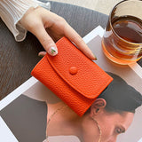 Porte carte en cuir synthétique orange tenu par une femme au-dessus d'un magazine de mode et à côté d'un verre de whisky.