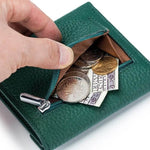 Une main ouvre la partie porte-monnaie du produit avec des pièces de monnaie et des billets dedans.