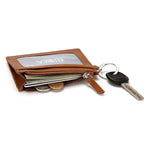 Le produit est allongé sur une table claire avec des clés attachées ainsi que des cartes, des billets et des pièces de monnaie dans son compartiment principal.
