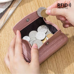 Le côté porte monnaie est ouvert avec des pièces dedans, dont deux retirées par une main de femme. le produit est sur une table en bois.
