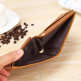 Une main ouvre le compartiment pour les billets du produit qui est mis sur une table en bois clair alors qu'on voit à la gauche de l'image une tasse de café blanche avec des fève de café à côté.