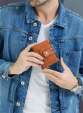 Un homme en t-shirt et veste en jeans tient un porte-cartes en cuir marron pour homme dans ses mains.