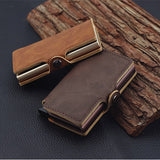 On voit les porte-cartes de crédit en cuir marron adossés à une tuile en bois qui est elle-même sur une surface noire.