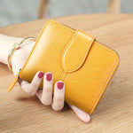 Une main féminine tient un porte-cartes en cuir pour femme dans sa main. Celui-ci est de couleur jaune.