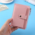 Porte-cartes en cuir rose tenu par une main avec une table bleue en fond.
