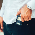 Un homme en chemise blanche retire son porte-cartes en cuir bleu de sa poche.